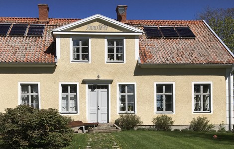 En stor gul herrgårdsbyggnad med vita knutar. På taket sitter sex stycken solpaneler och längst upp på husfasaden kan man läsa texten Anno 1849.  