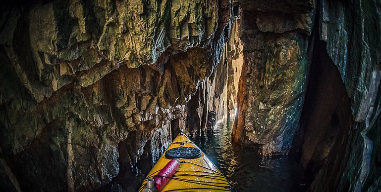 En bild inifrån Rödgavels grotta. På bilden ser man en gul kajak som är inne i en grott öppning.  