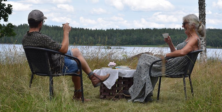 En kvinna och man som sitter och dricker te framför en sjö. 
