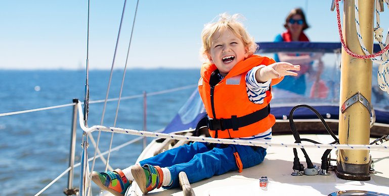 En glad pojke med flytväst som sitter på en segelbåt.